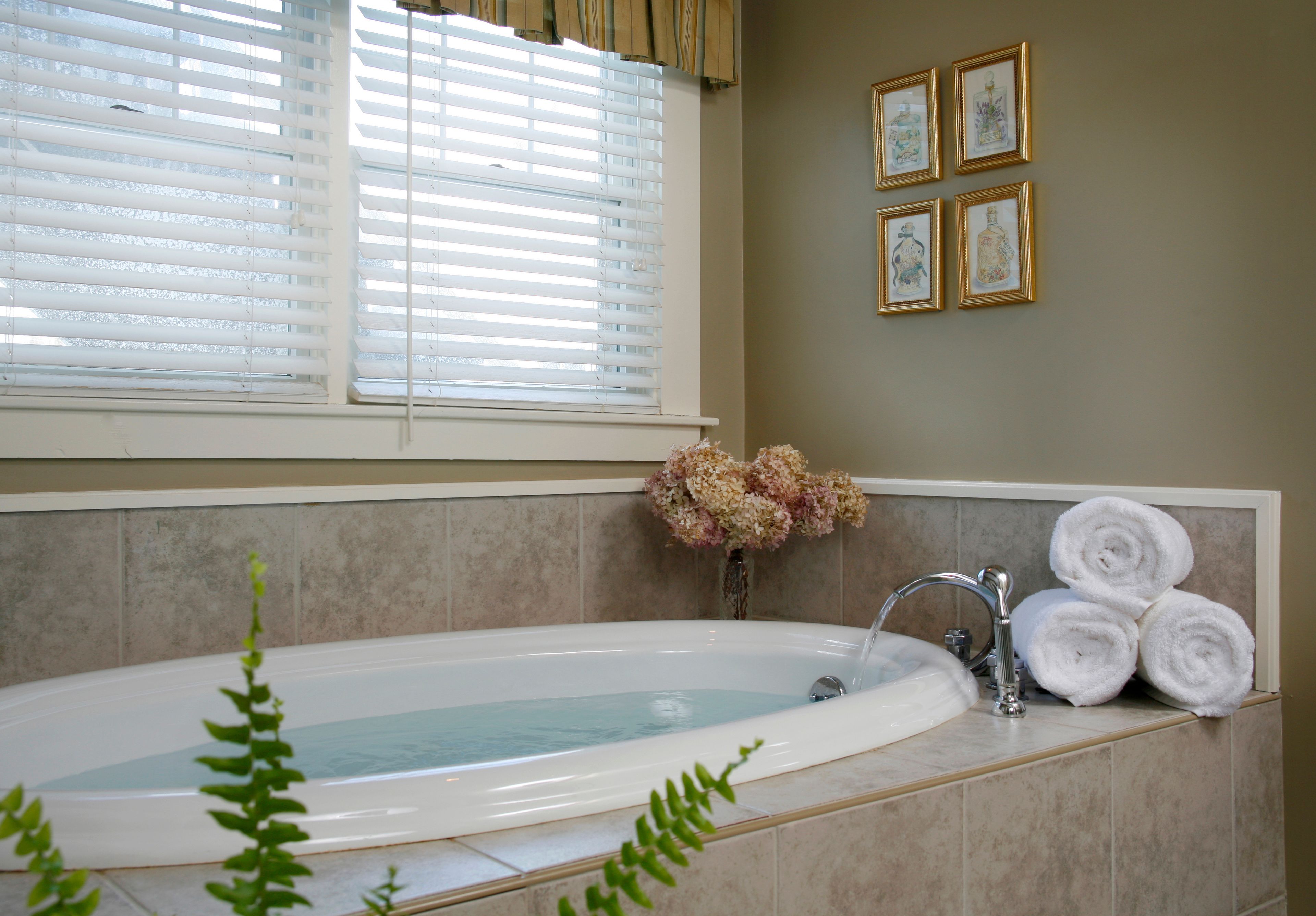 Un baño con una bañera, una ventana con persianas, un lavabo y toallas.