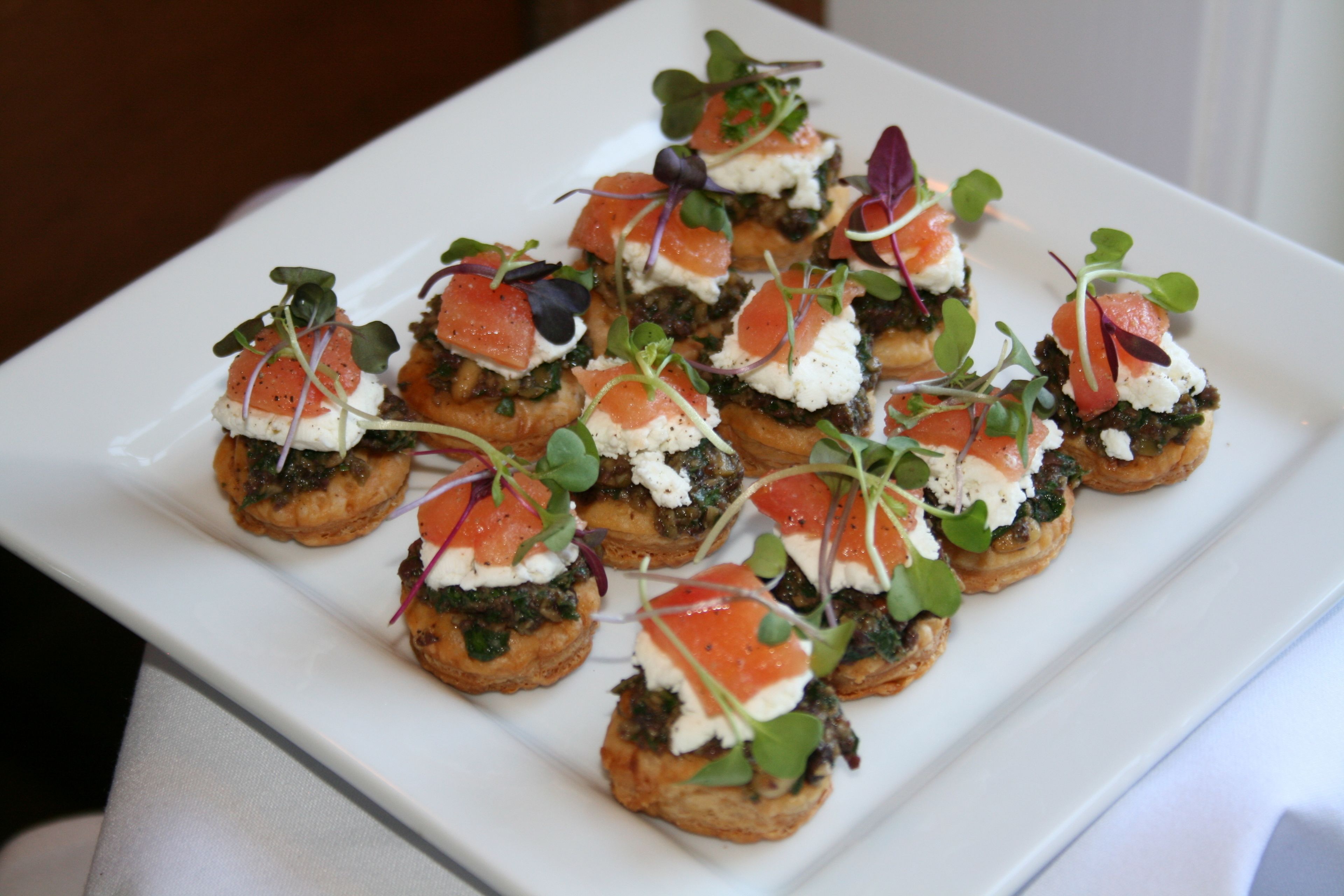 A white rectangular plate with several appetizers arranged in a grid pattern.