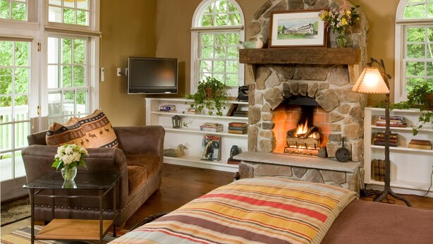 A spacious living room with a stone fireplace, wooden beams, and large windows. - Sugar Hill Inn (Sugar Hill)