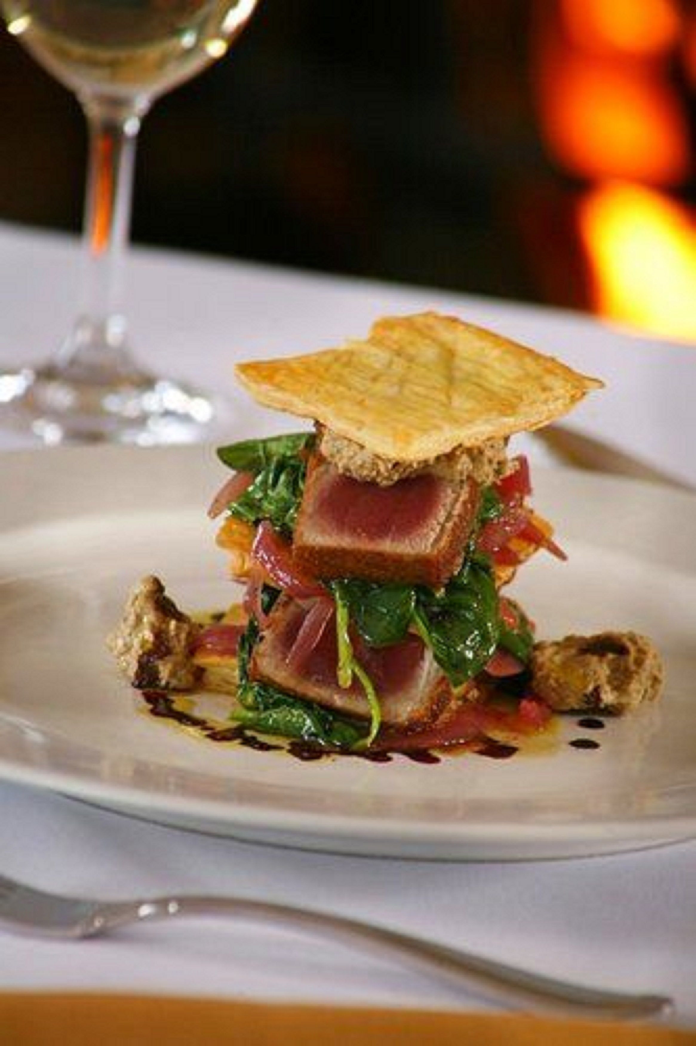 A dish with a crispy base, layered with greens, meat, and a sauce, served on a white plate.