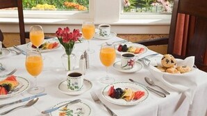 A breakfast setting with a table set for two, featuring plates of fruit, juice glasses, and a small bowl of muffins. - Sugar Hill Inn (Sugar Hill)