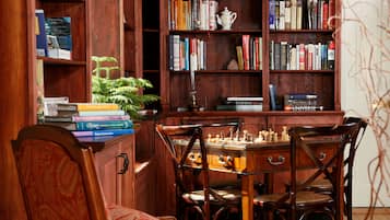 Una estantería de madera llena de libros, un tablero de ajedrez y una pequeña planta.