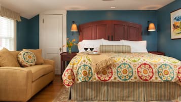 A bedroom with a large bed, a sofa, a nightstand with two lamps, and a window with curtains.