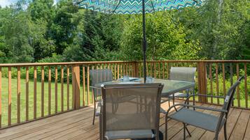 A wooden deck with a table and chairs, an umbrella, and a view of a forested area.