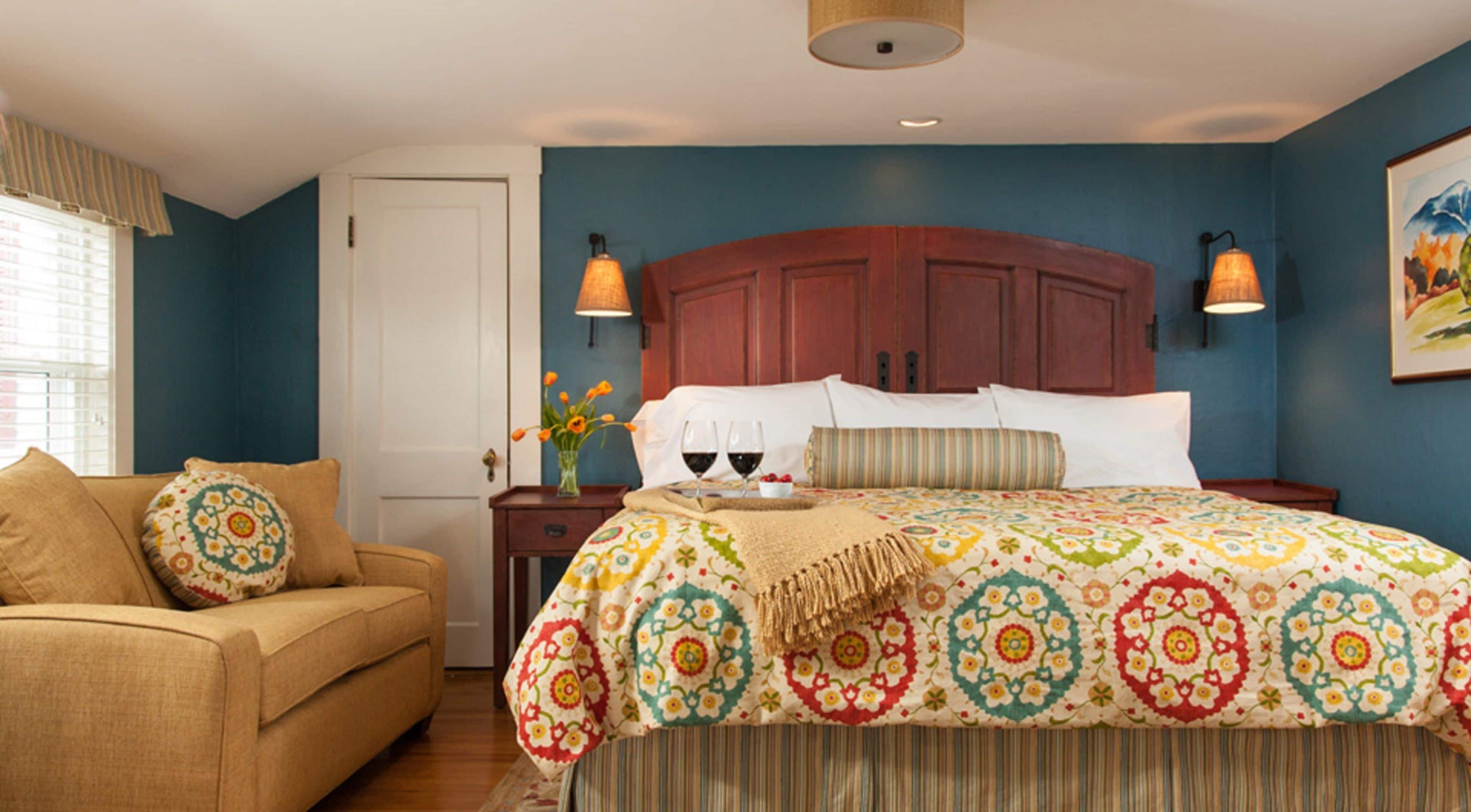 A bedroom with a large bed, a wooden headboard, two bedside lamps, a nightstand, a sofa, and a window with curtains.
