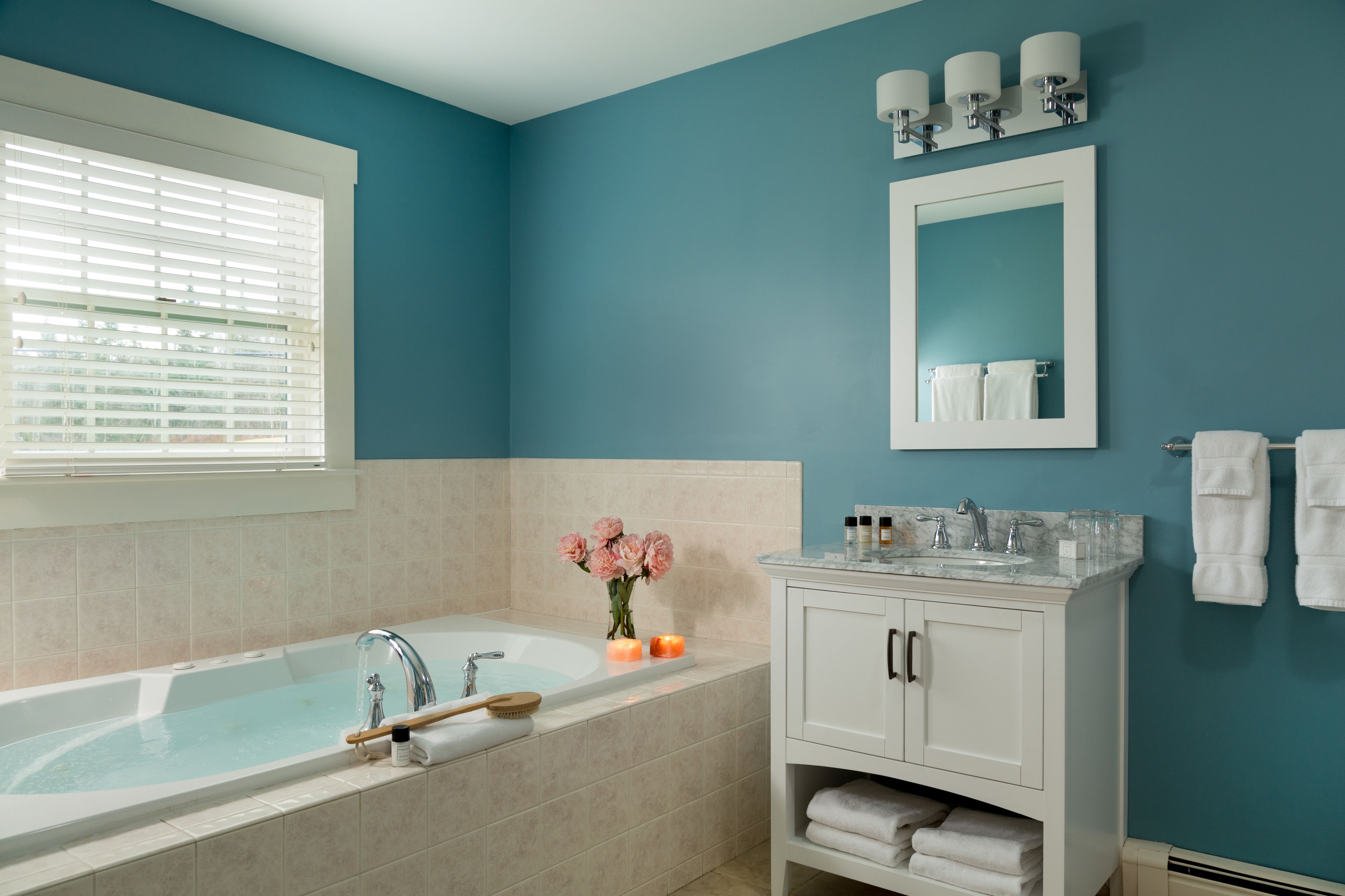 A modern bathroom with a bathtub, a vanity with a mirror, and a window with blinds.