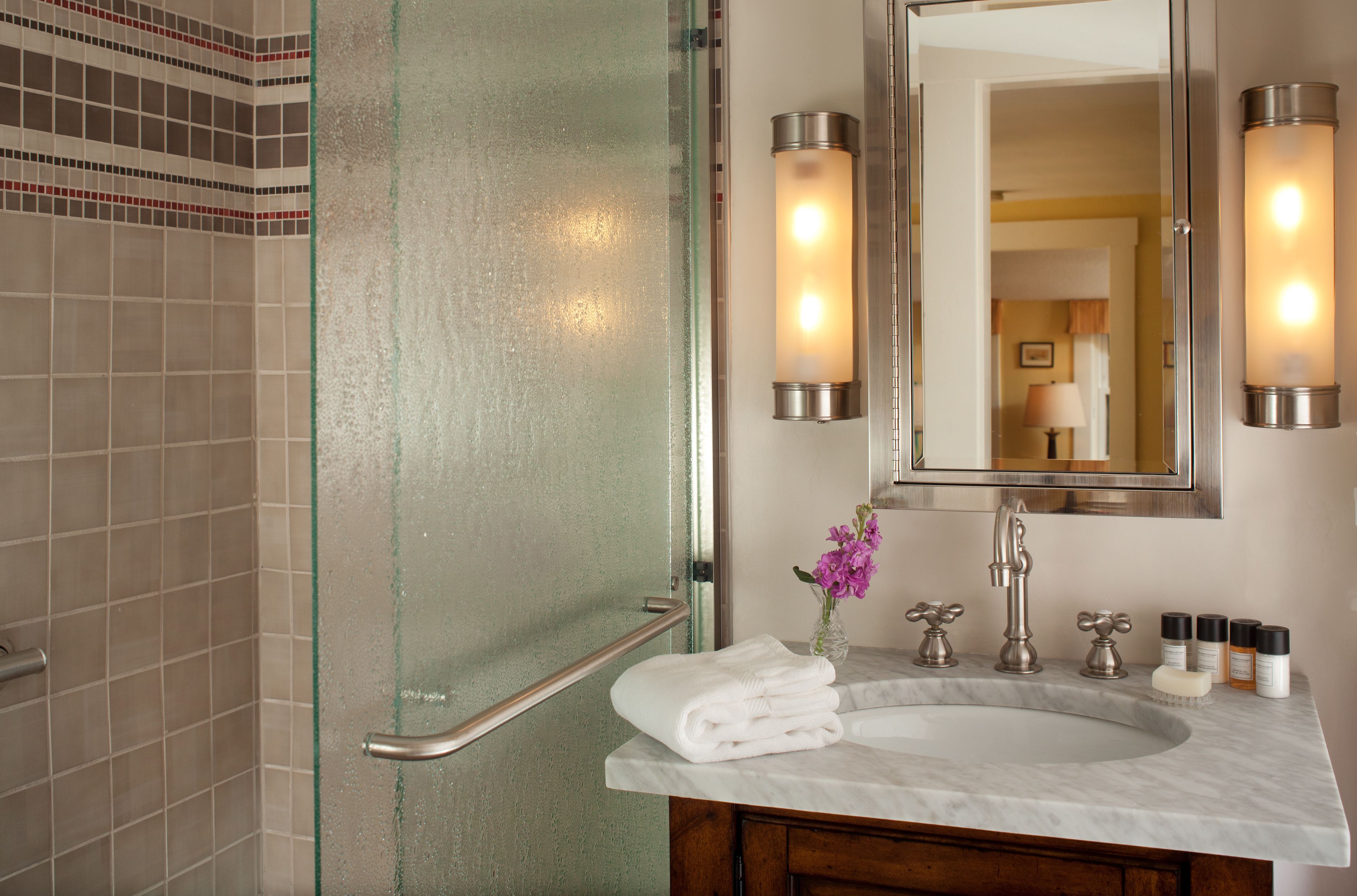 A bathroom with a glass shower door, a marble sink, and a mirror with wall sconces.