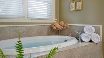 A bathroom with a bathtub, a sink, and a window with blinds. There are towels and a vase with flowers on the counter.
