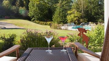 A patio with two chairs and a table, overlooking a grassy area with a pool and a decorative moose head.