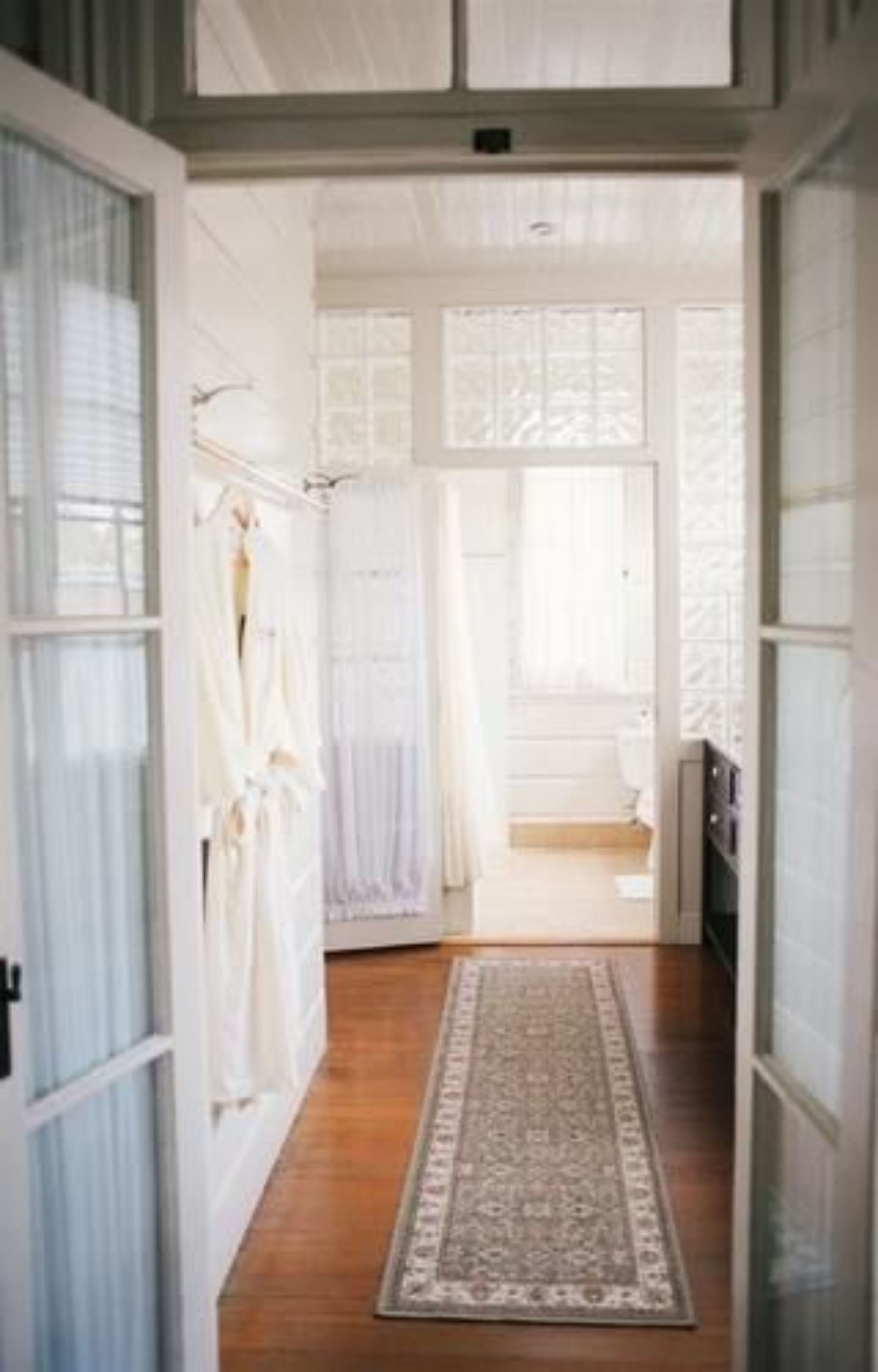 A hallway with a wooden floor, a patterned rug, and a view into a room with a bed and a window.