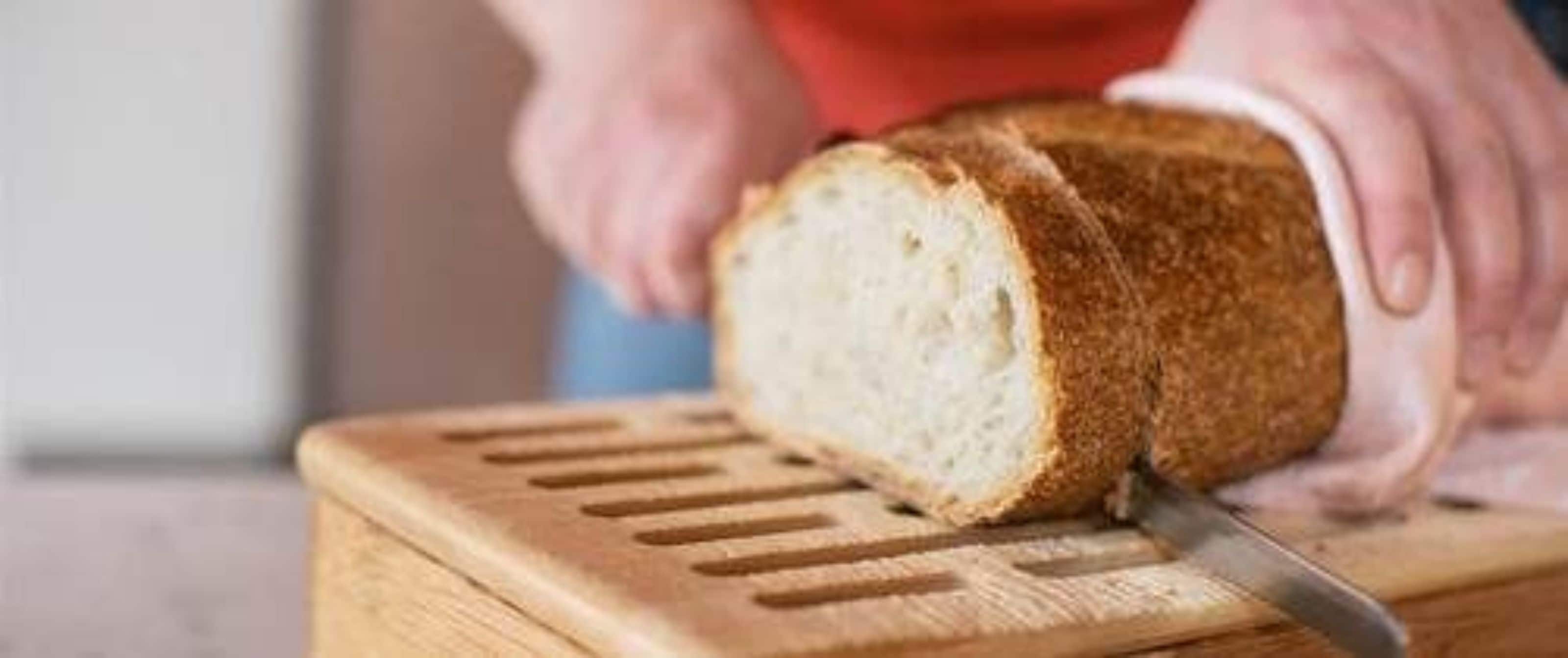 On voit une miche de pain qu’on tranche sur une planche à découper en bois.