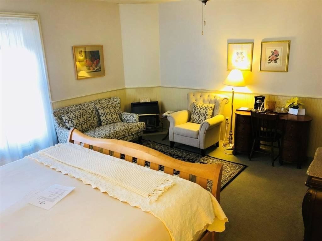 A hotel room with a bed, a sofa, a chair, a desk, and a lamp.