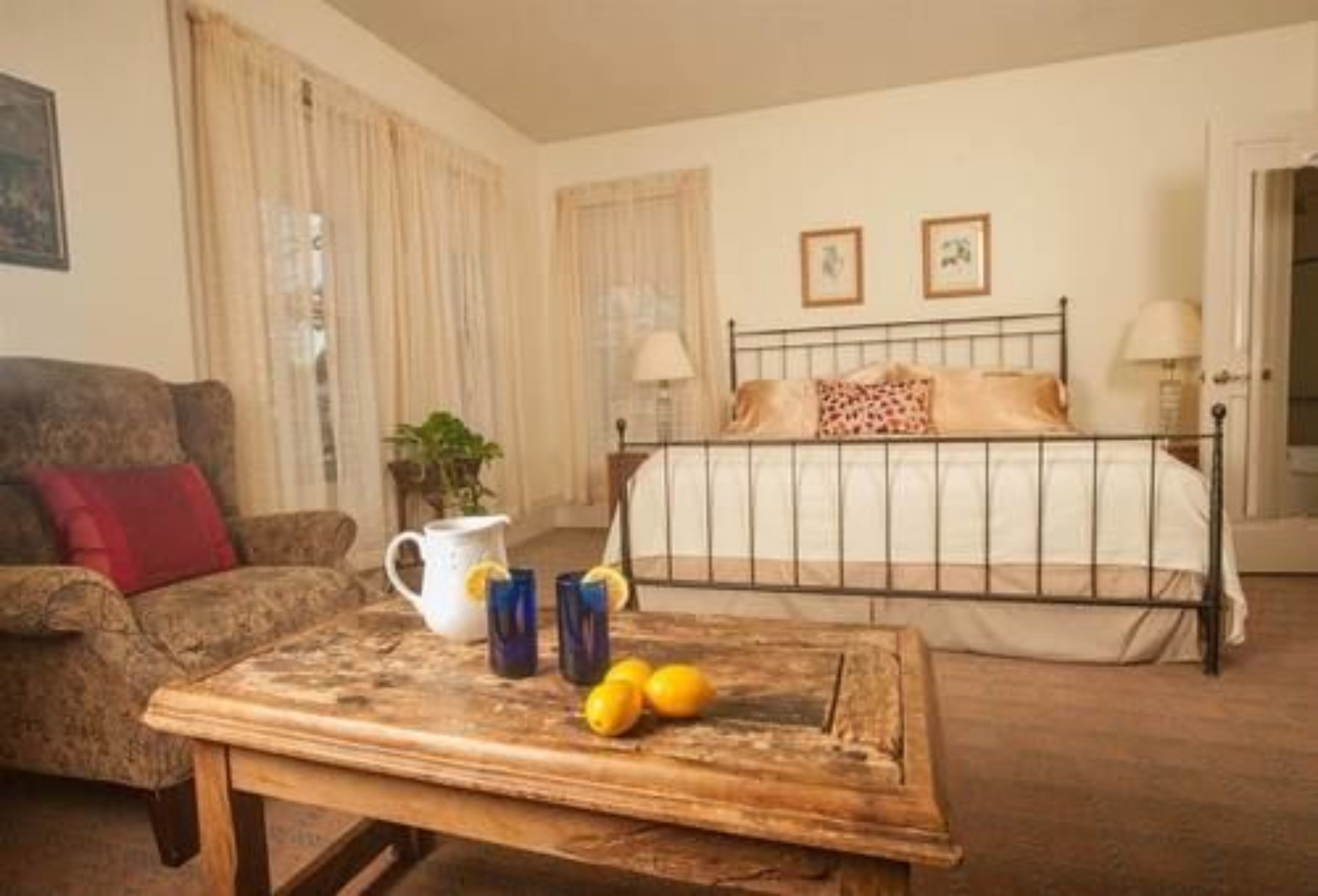 Une chambre à coucher avec un lit, une table en bois sur laquelle se trouvent une carafe et des citrons, un canapé et des rideaux.