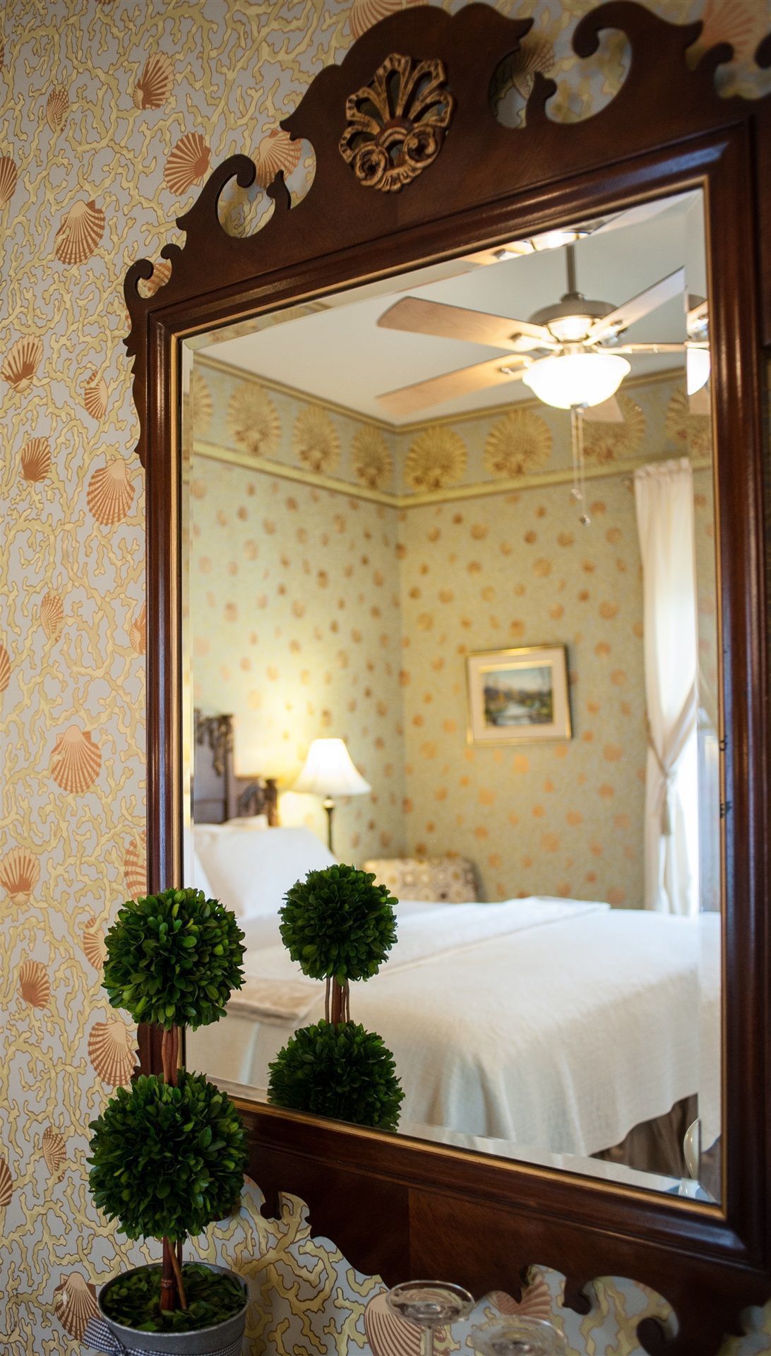 A bedroom with a bed, a ceiling fan, and a mirror reflecting the room.