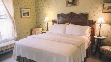 A traditional bedroom with a large bed, two bedside tables, and a window with curtains.