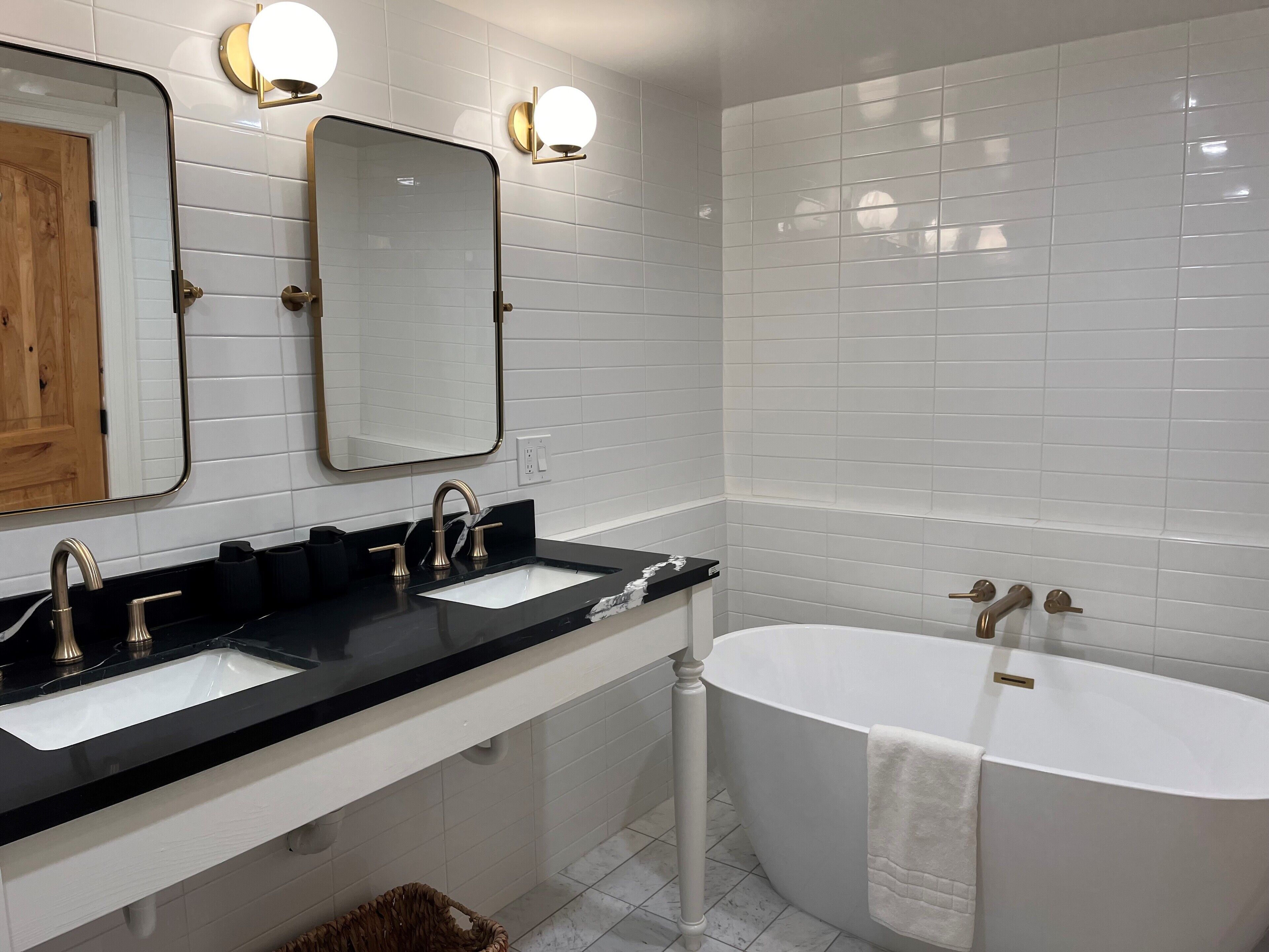 A modern bathroom with two sinks, a large bathtub, and a mirror with wall-mounted lights.