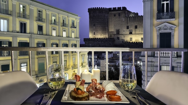 Taula de menjador amb un plat de menjar, gots de vi i una espelma. Al fons, es pot veure un castell.