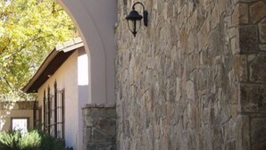 A stone building with a white facade and an arched entrance. There are two wall-mounted lanterns and a metal gate at the entrance.