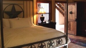 A four-poster bed with a star design, a nightstand with a lamp, and a wooden door in a room with a tiled floor.