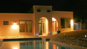 A modern house with a swimming pool, a well-lit entrance, and a stone pathway leading to the door.