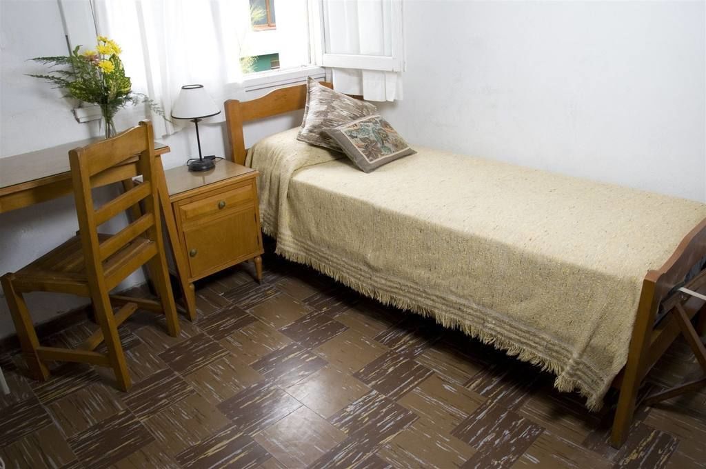 Un dormitorio pequeño y ordenado con una cama de madera, una mesita de noche, una silla y un escritorio.