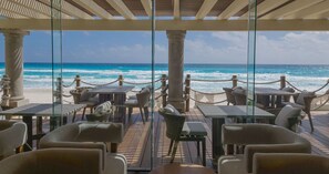 Un restaurante frente a la playa con terraza, vistas al océano y una estructura de pérgola.