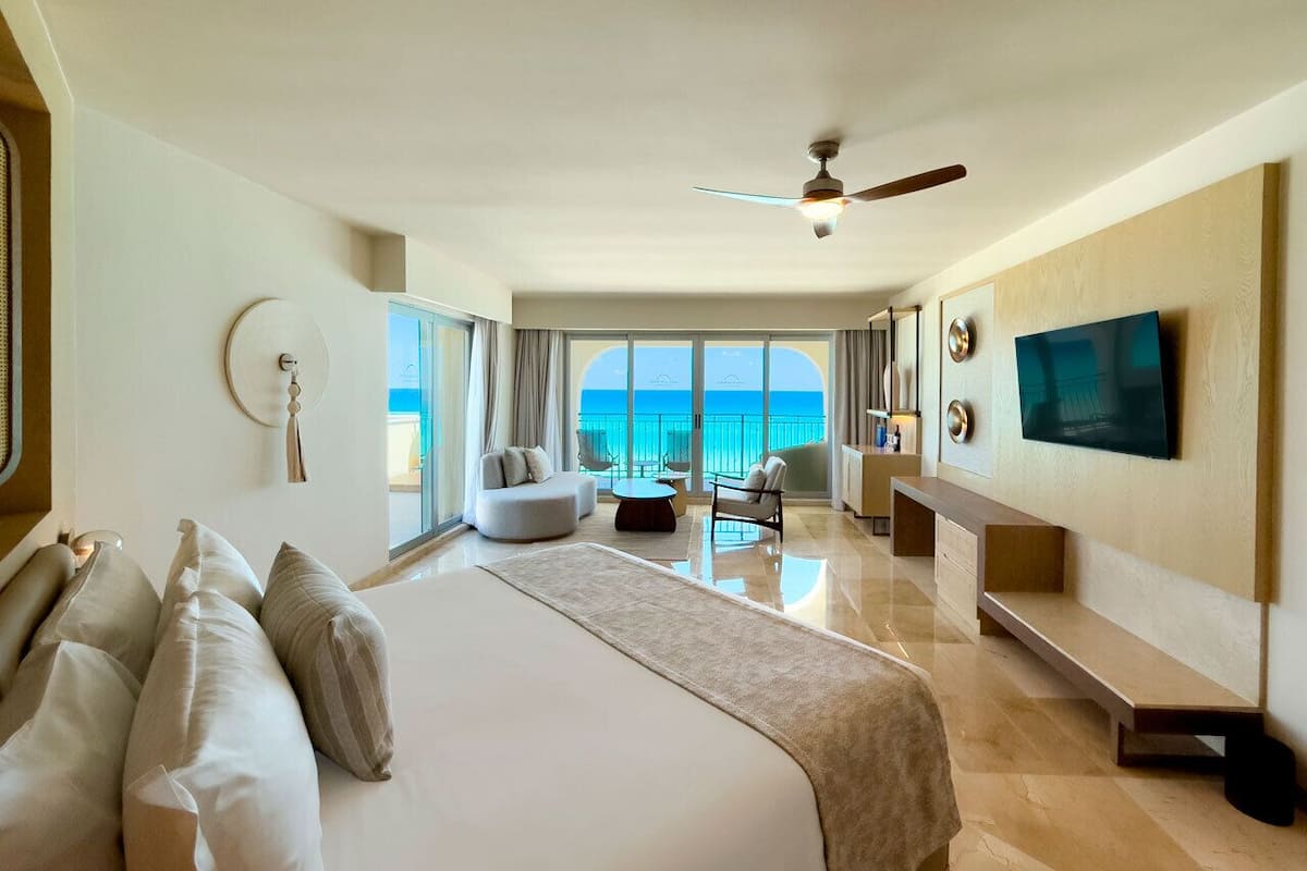 Ein geräumiges Hotelzimmer mit großem Bett, einer Sitzecke, einem Fernseher und Blick aufs Meer.