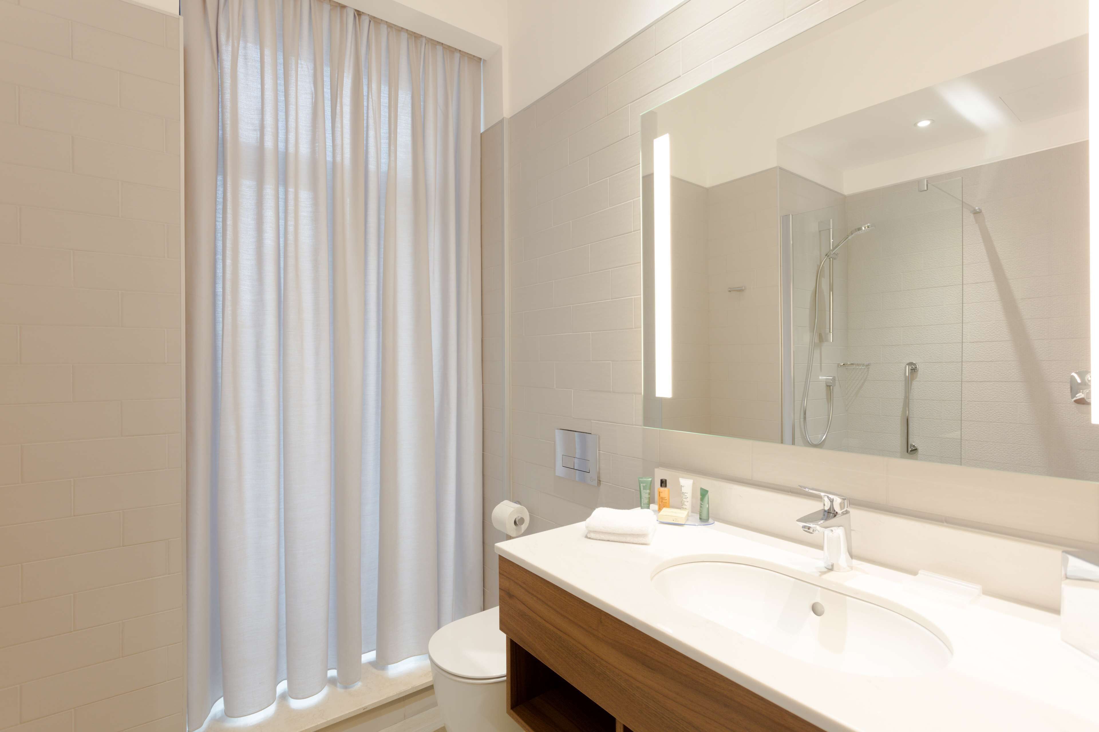 A modern bathroom with a large mirror, a white sink, and a shower area.