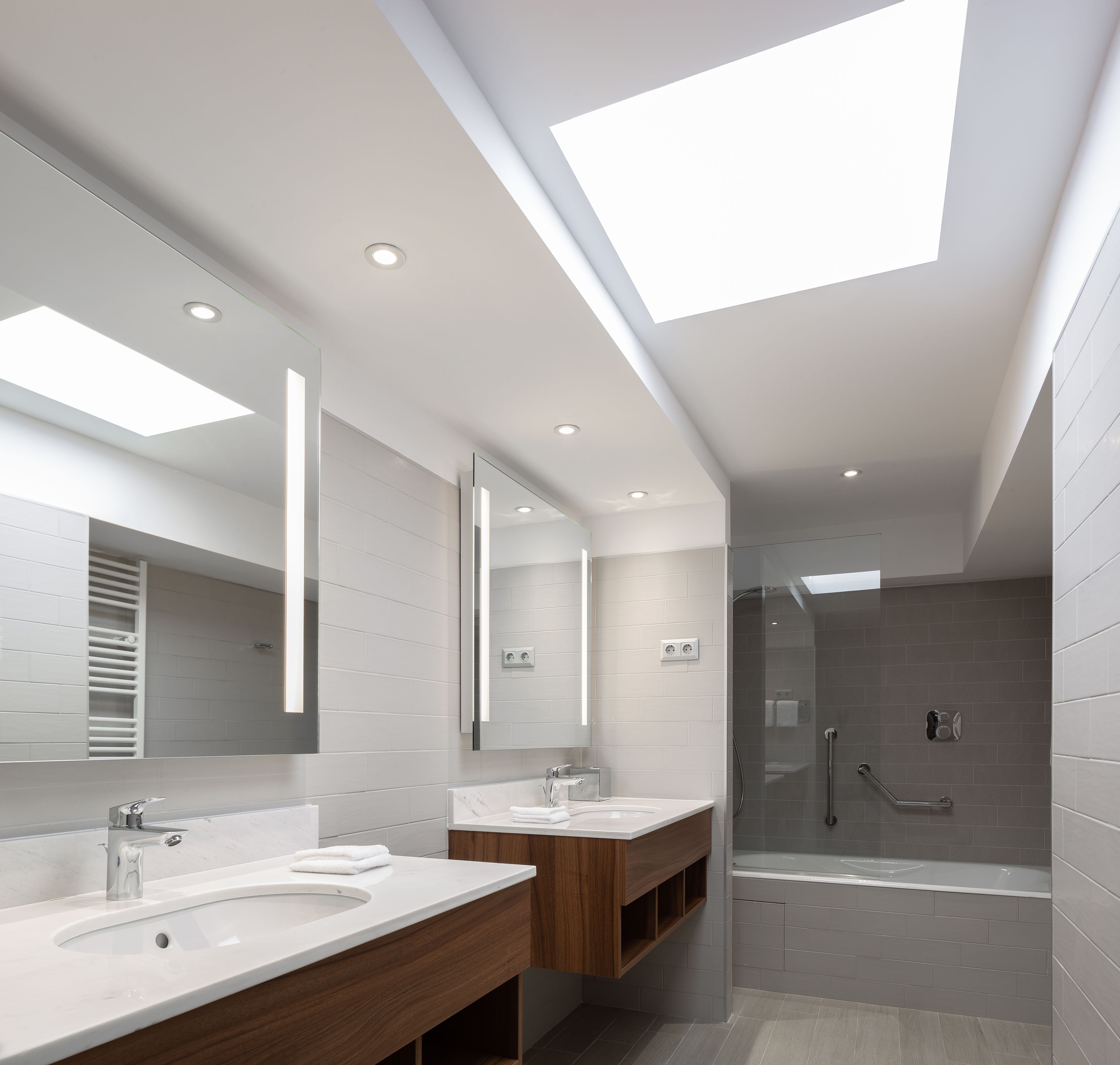 Un baño moderno con dos lavamanos, un espejo grande y una ducha con mampara de cristal.