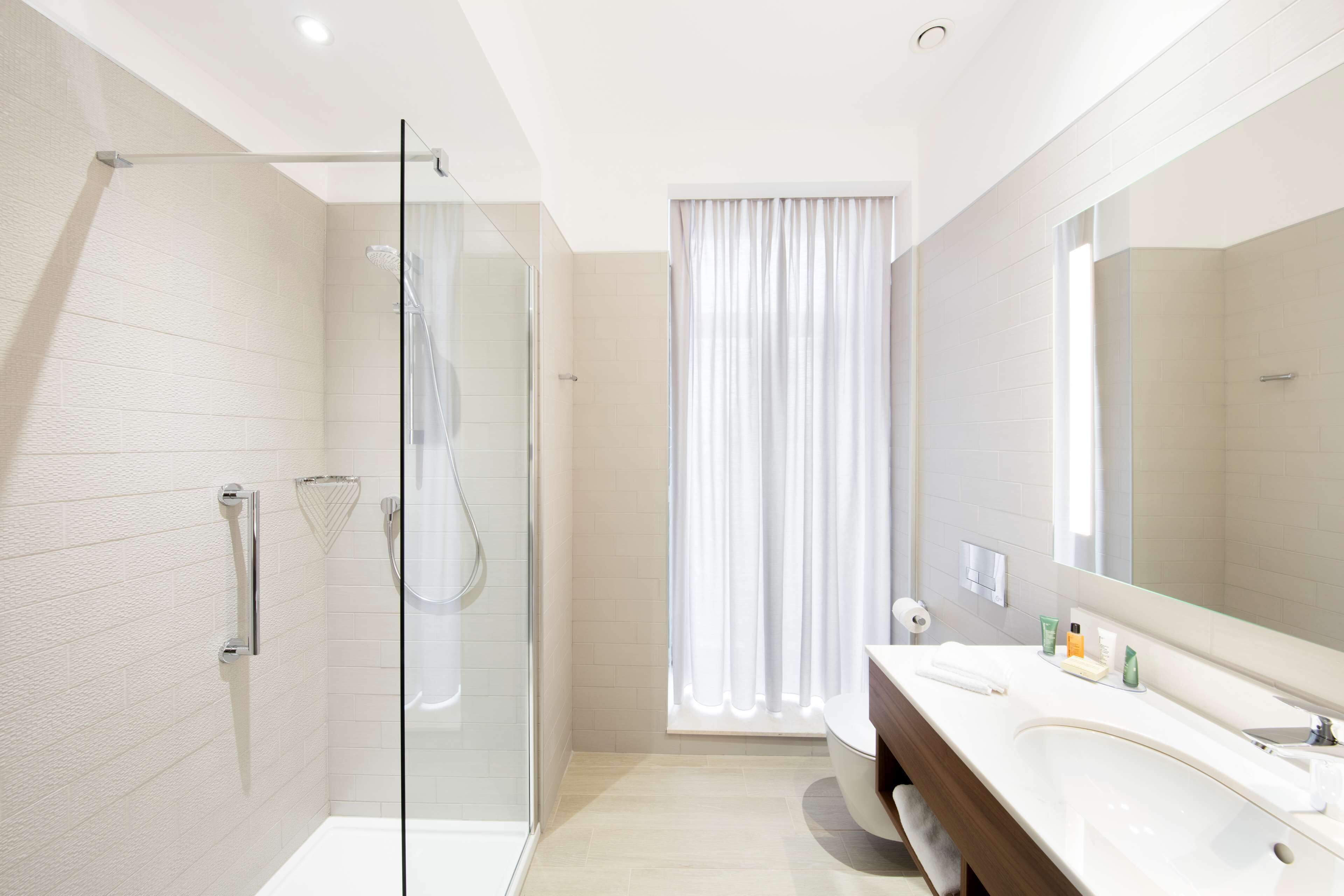 A modern bathroom with a glass shower enclosure, a large mirror, and a vanity with toiletries.