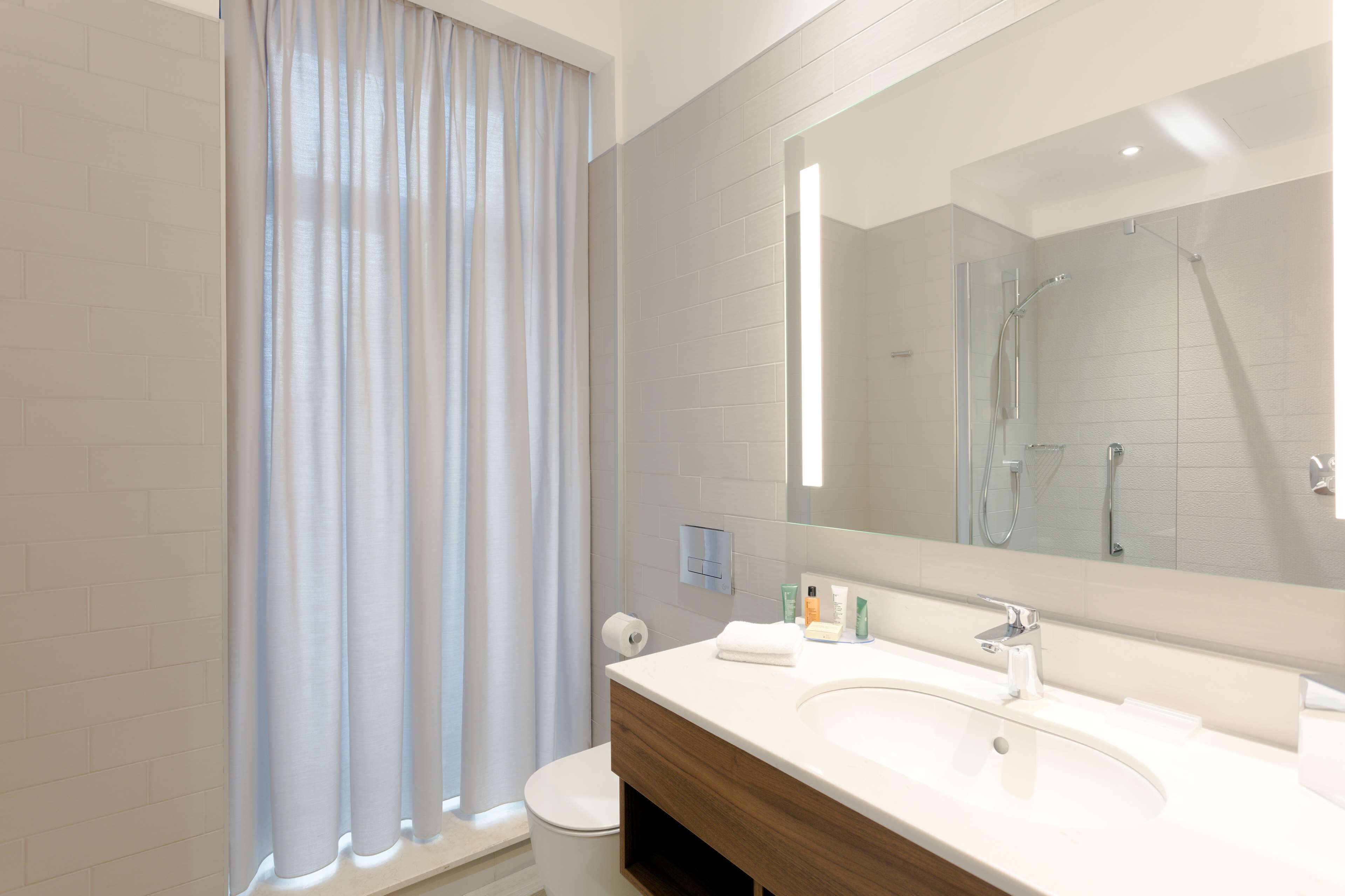 Un baño moderno con un espejo grande, lavamanos blanco y zona de ducha.