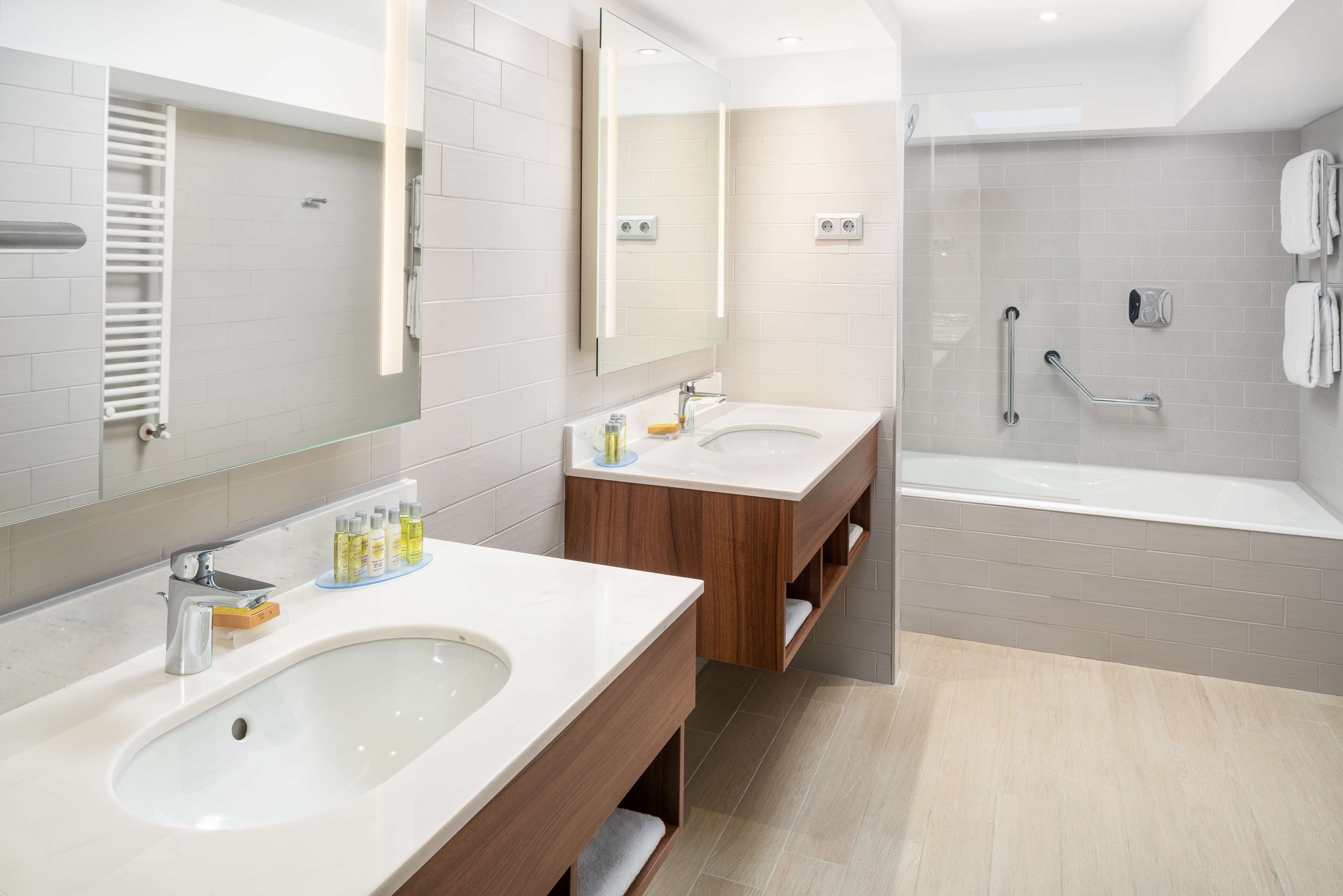 Un baño moderno con dos lavamanos, un espejo grande, una ducha con mampara de vidrio y un perchero para toallas.