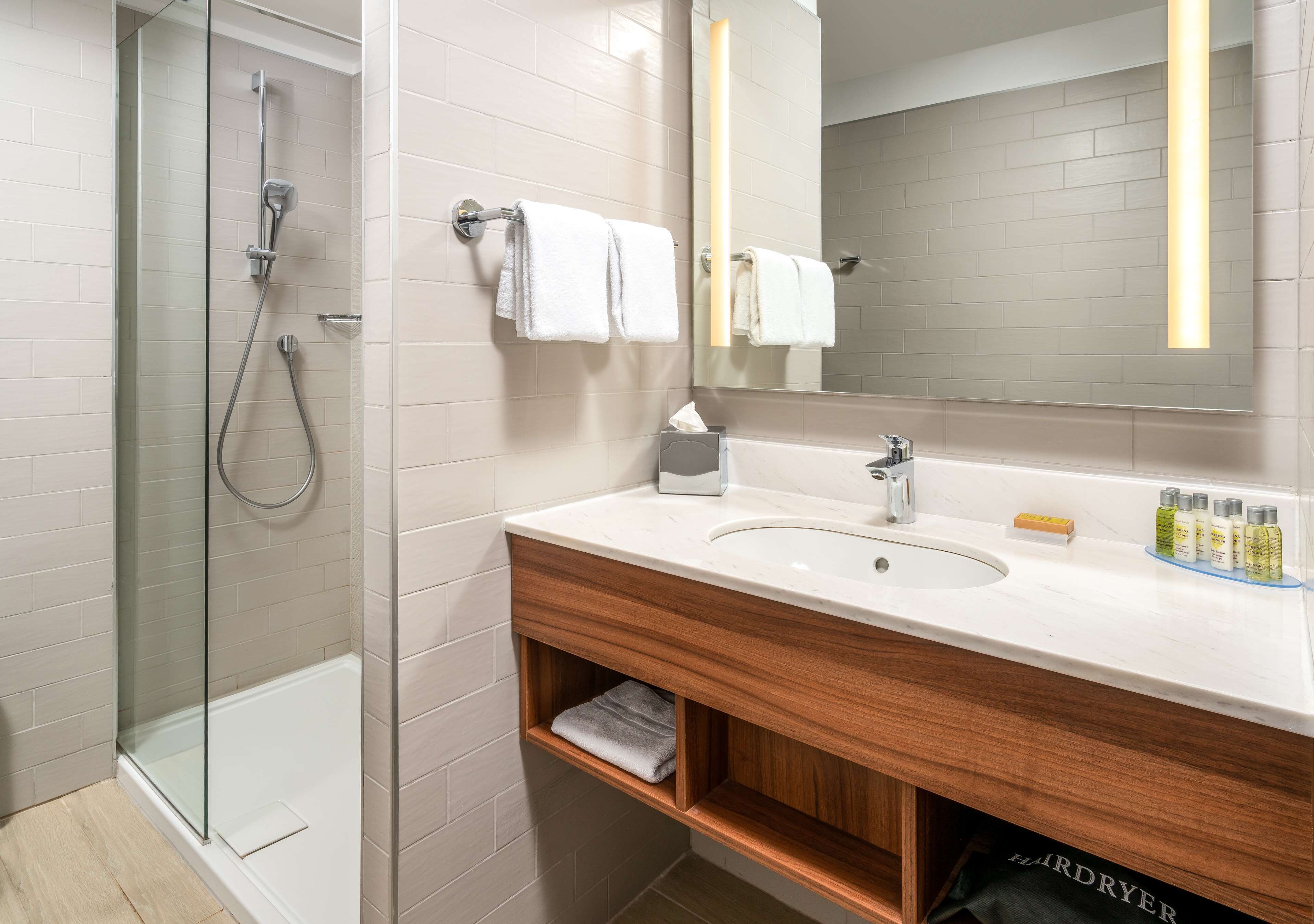 A modern bathroom with a glass-enclosed shower, a white sink with a wooden vanity, and a large mirror.