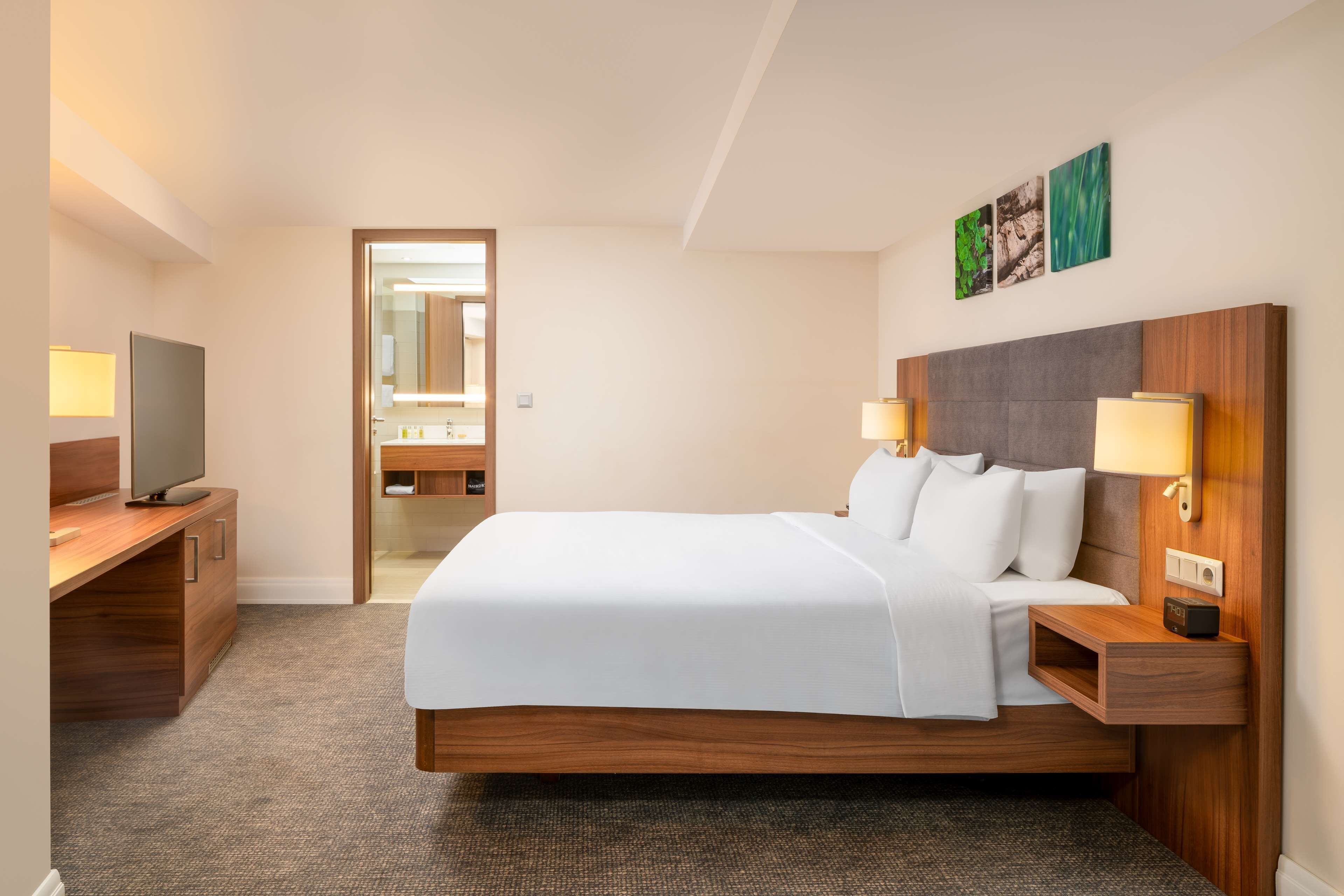 A hotel room with a large bed, bedside lamps, a TV, and a desk.