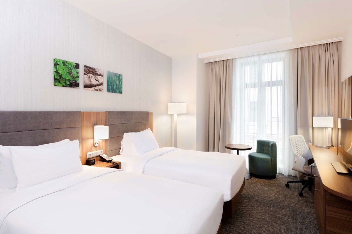 A hotel room with two beds, a desk, a chair, and a small table.