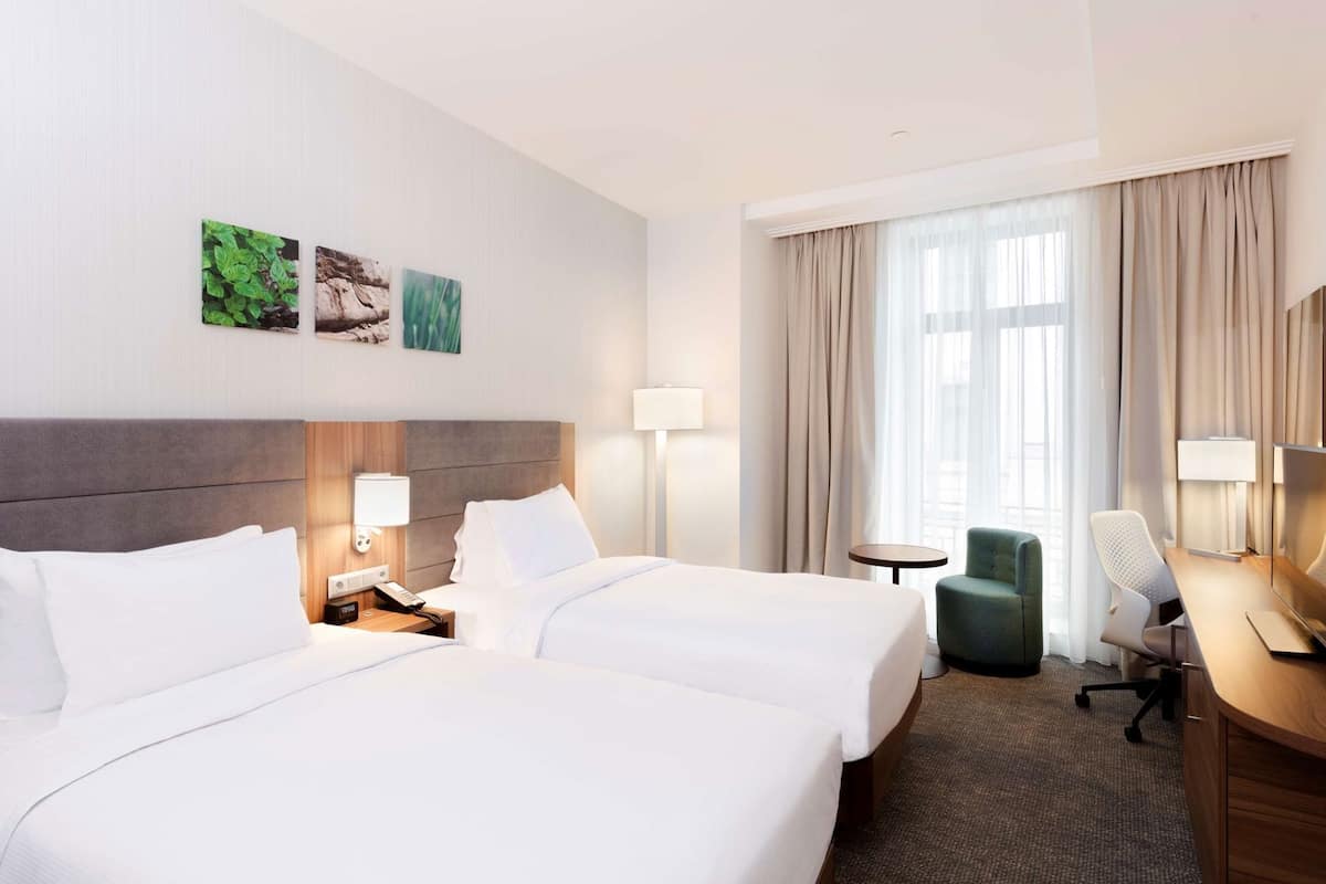Ein Hotelzimmer mit zwei Betten, einem Schreibtisch, einem Stuhl und einem kleinen Tisch.