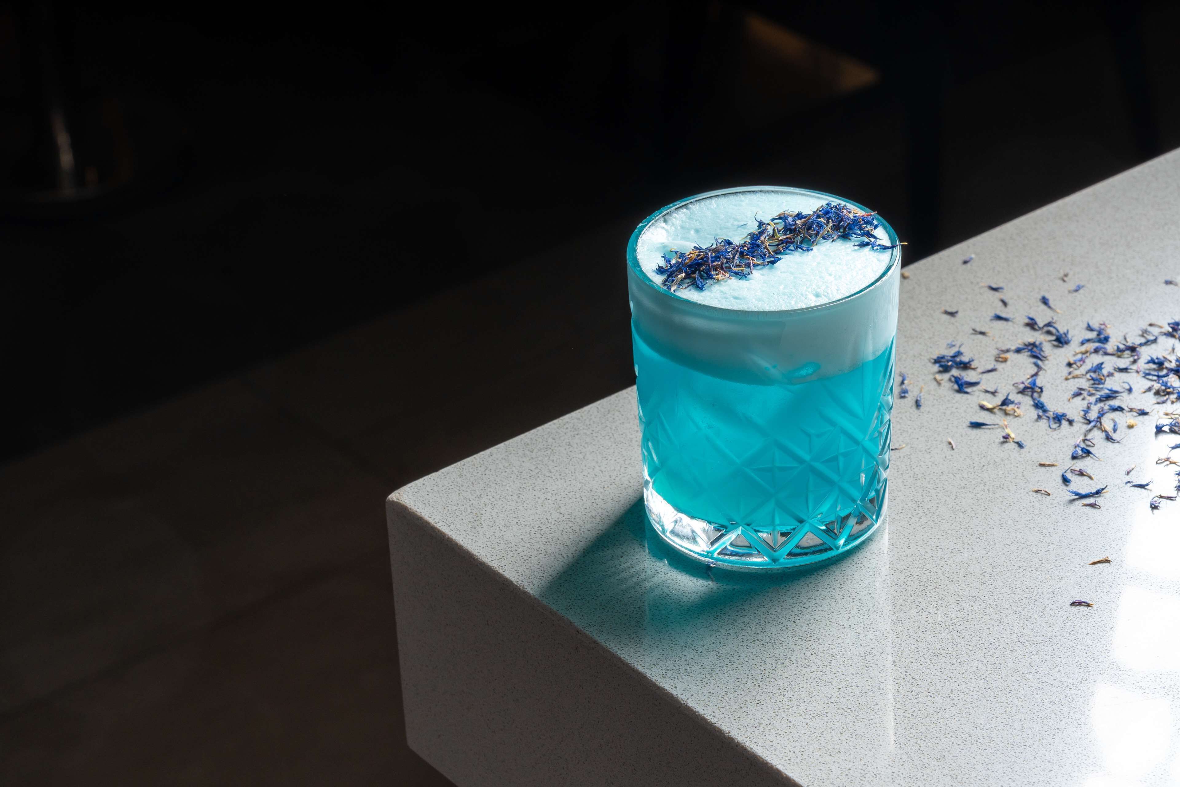 A glass of blue liquid with a textured pattern, placed on a light-colored surface.