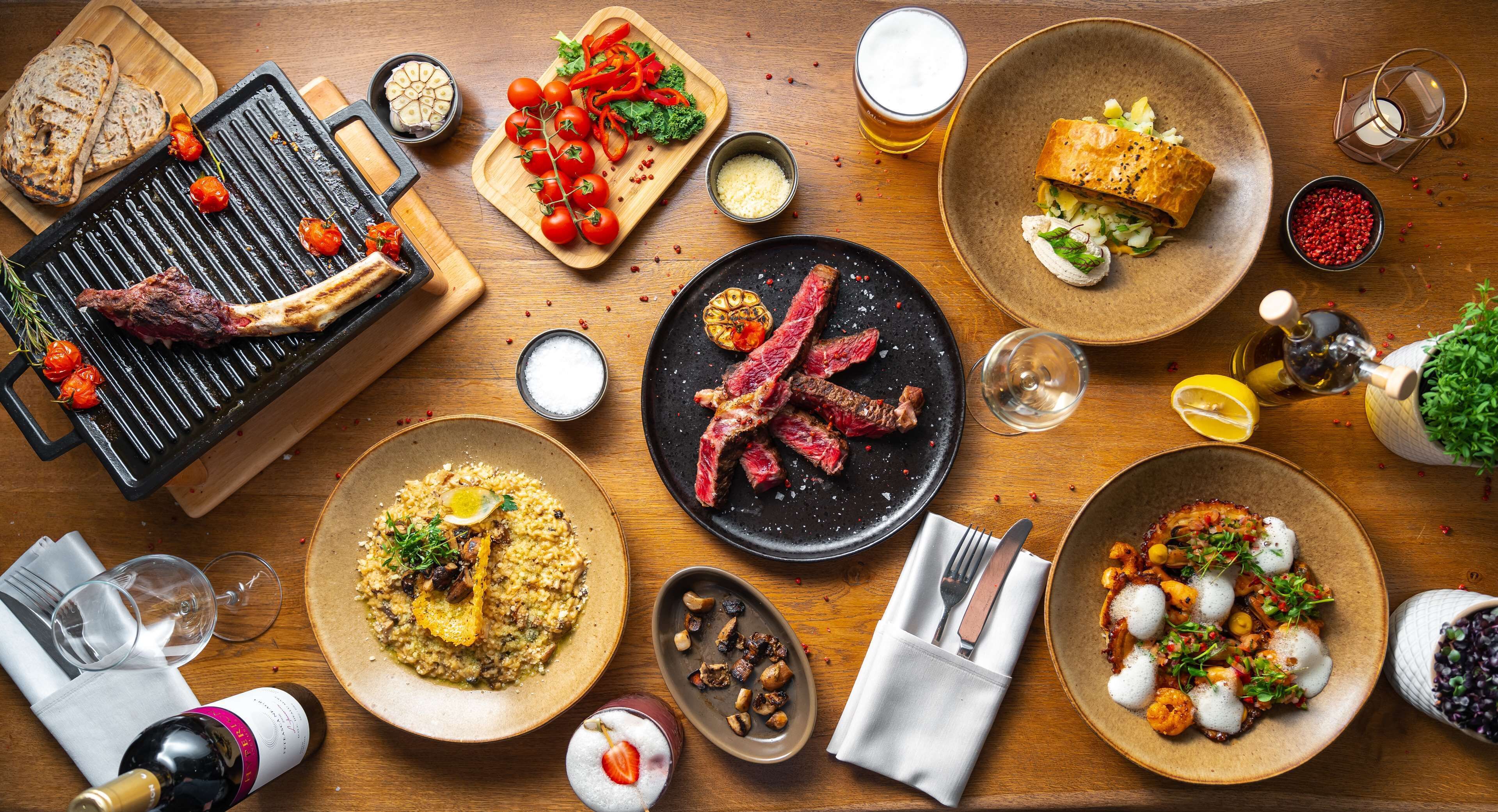 Une table à manger avec divers plats, notamment de la viande grillée, des salades et du pain.