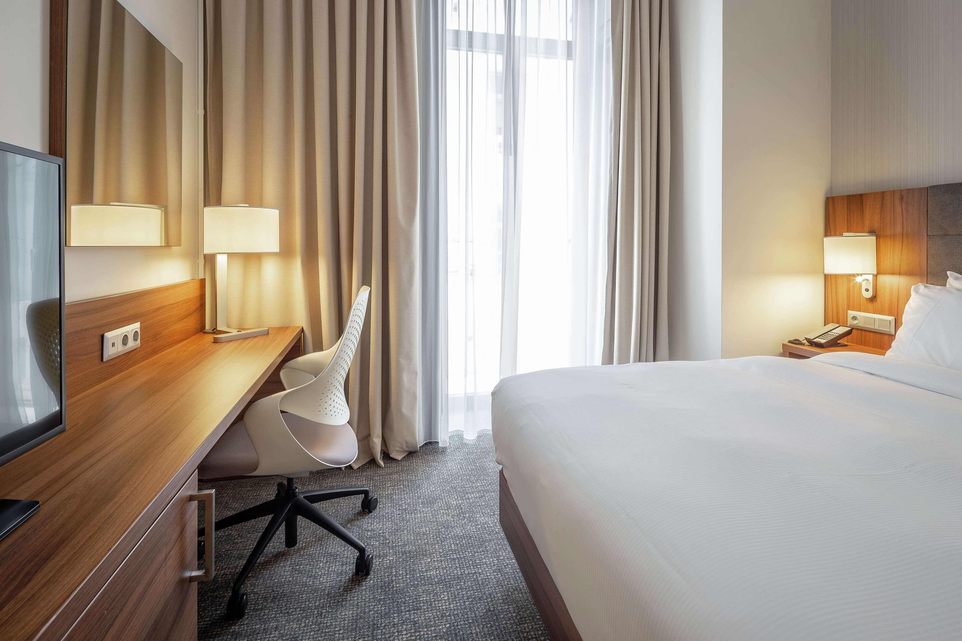 A hotel room with a bed, a desk with a chair, a TV, and two bedside lamps.