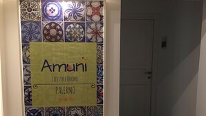 A sign with the name "Amuni" and the text "Lifestyle Rooms Palermo" on a wall with a decorative tile pattern. - Amunì - Palermo (Palermo)