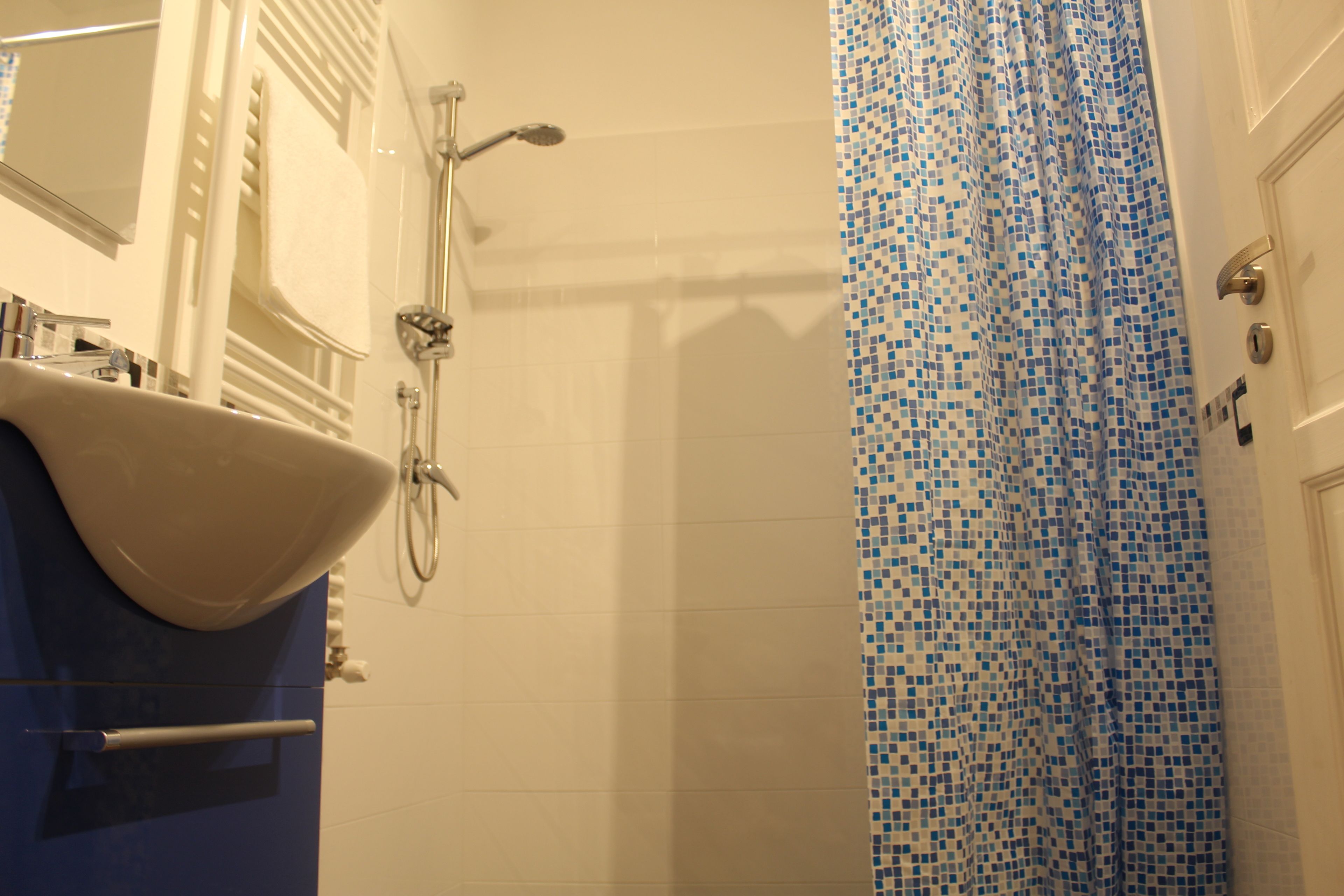 Une salle de bain avec un lavabo blanc, un miroir, une douche et un rideau de douche bleu à motifs de mosaïque.
