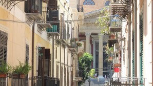 A narrow street with buildings featuring balconies, some with plants, and a mosque in the background. - Amunì - Palermo (Palermo)