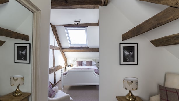 A bedroom with a sloped ceiling, a skylight, a bed, a chair, a table, and two framed pictures on the walls.