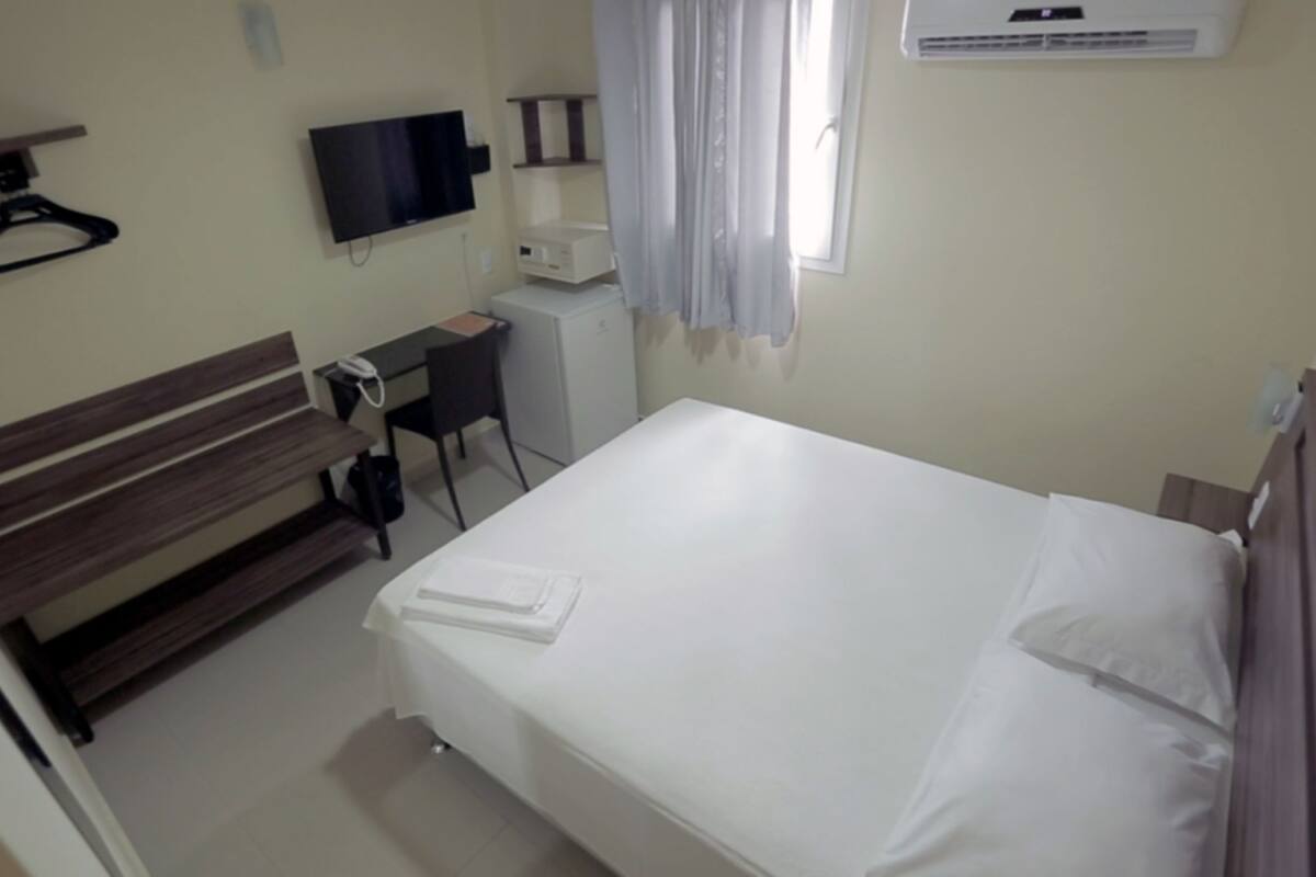 Una habitación de hotel con una cama, un escritorio, una silla, un televisor y aire acondicionado.
