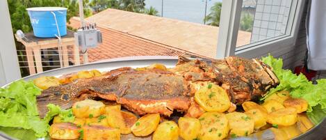Una bandeja de mariscos con pescado y papas sobre una mesa, con vista al mar y edificios al fondo.