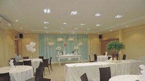 A banquet hall with round tables, chairs, and a stage with a backdrop. - Sandis Mirante Hotel (Santarém)