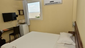 A hotel room with a bed, a desk, a chair, a TV, an air conditioner, and a window with a view of the sea. - Sandis Mirante Hotel (Santarém)