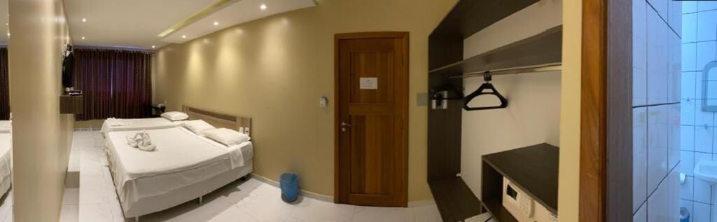 Une chambre d’hôtel avec deux lits, une porte en bois, un porte-manteau et une salle de bain équipée d’un lavabo et d’un miroir.