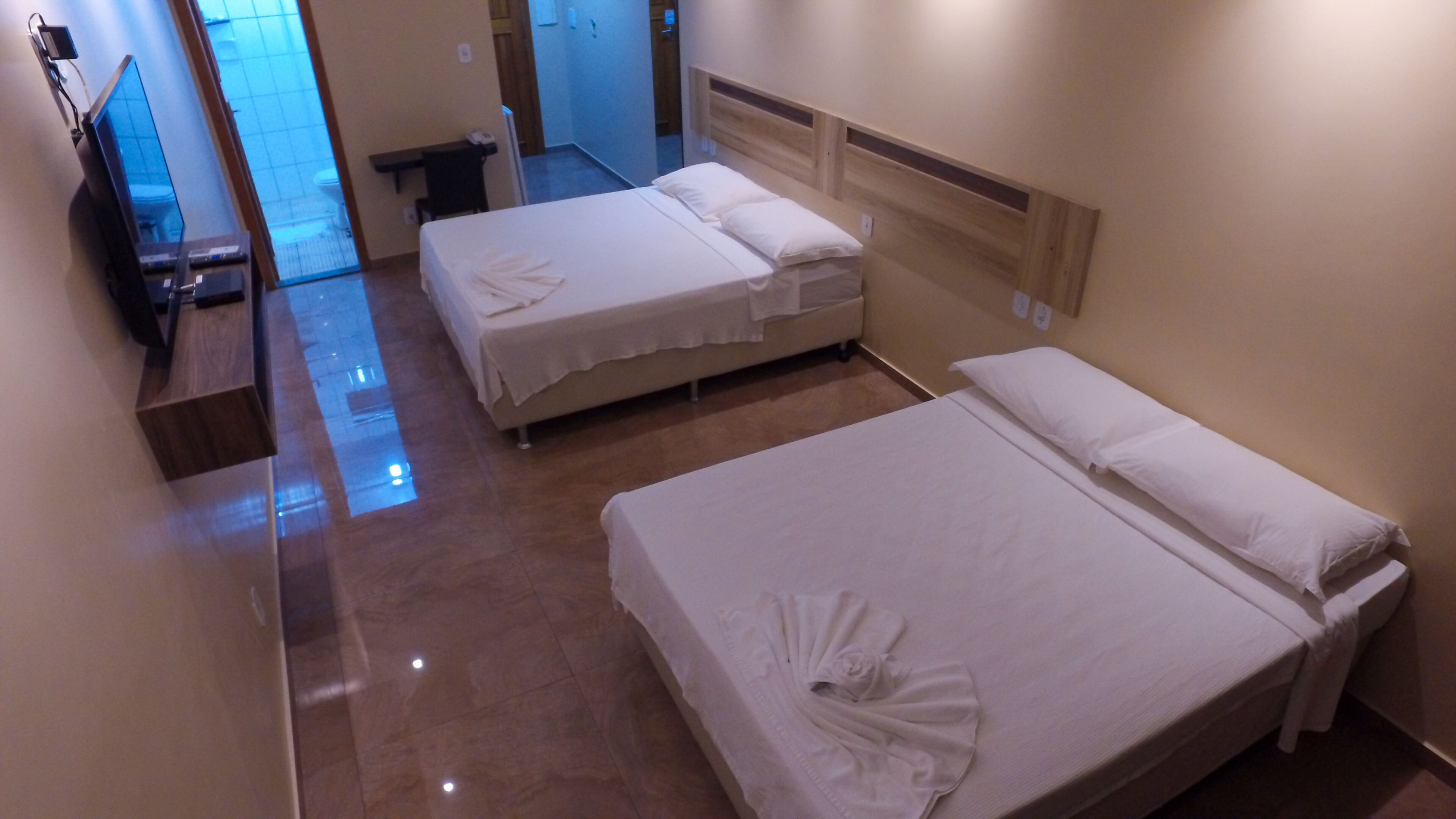 Quarto de hotel com duas camas, uma televisão e um banheiro ao fundo.