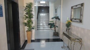 Un vestíbulo de hotel con una escalera, plantas en macetas, una consola con espejo y un suelo de baldosas.